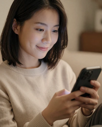 Asian woman smiling while reading a thoughtful first message on her dating app, warm indoor lighting