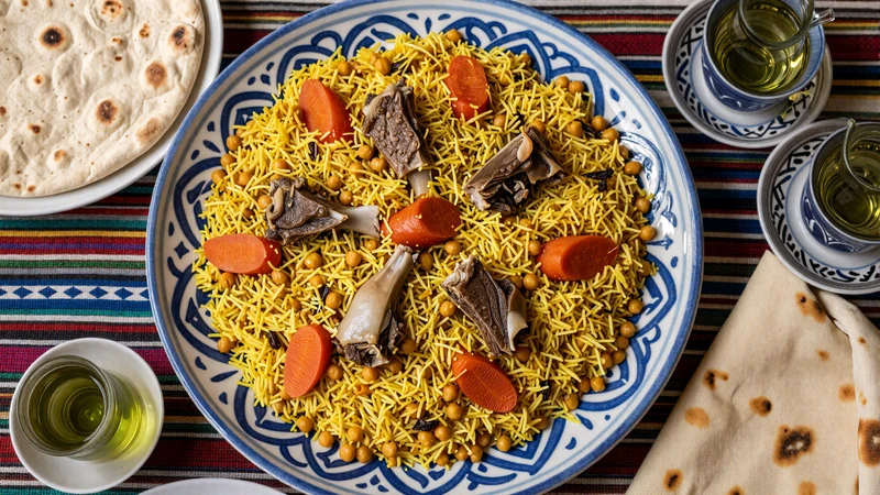 Traditional Uzbek plov rice dish with lamb and carrots served on ornate ceramic plate alongside flatbread and green tea
