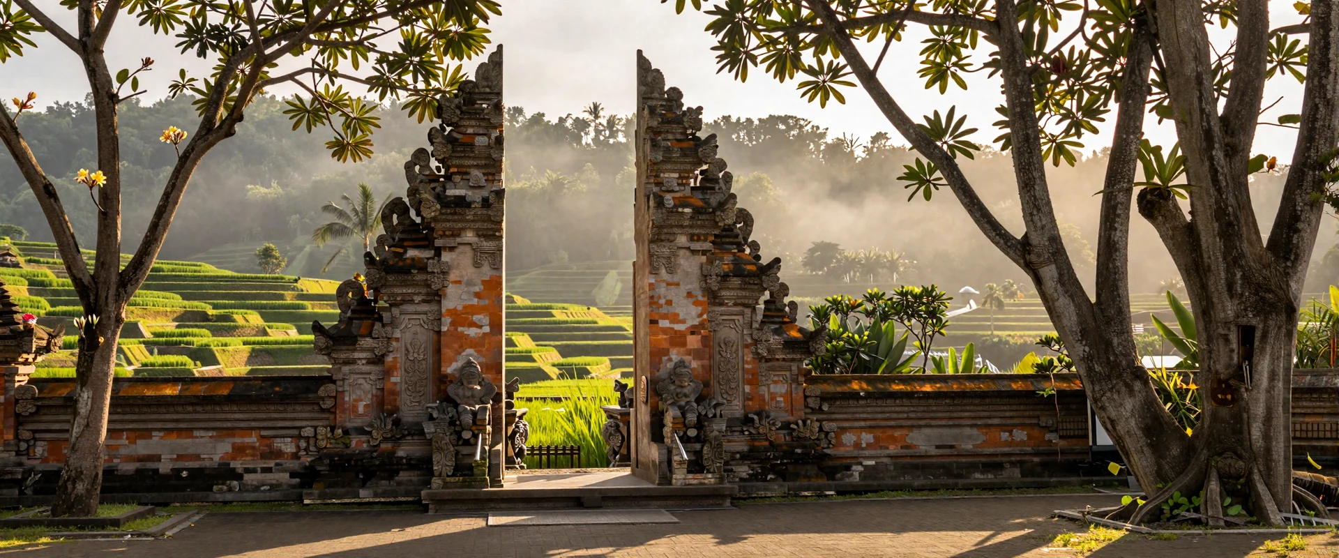 Balinese temple gateway surrounded by tropical frangipani trees with emerald rice terraces at golden hour in Indonesia